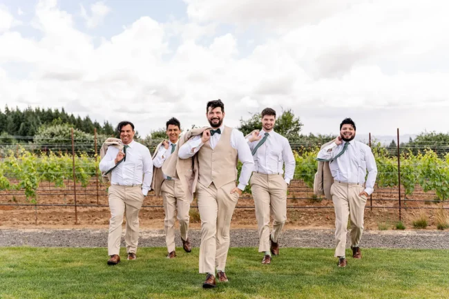 The groomsmen walking with a vineyard view behind them