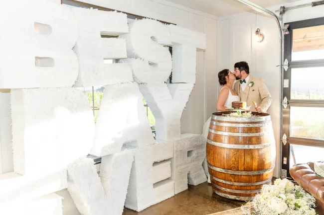 Bride and groom kissing after their cake cutting on a wine barrel with a Best Day Ever large sign