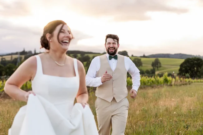 Bride and groom running through the field laughing